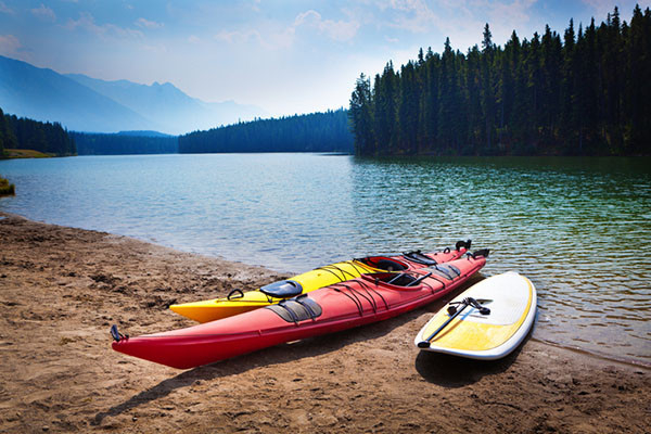two kayaks and a paddle board on the beach adjacent to a lake